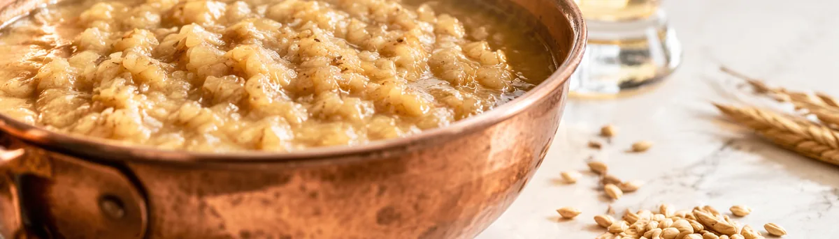 Cooked grain mash in a copper pan with wheat grains beside it